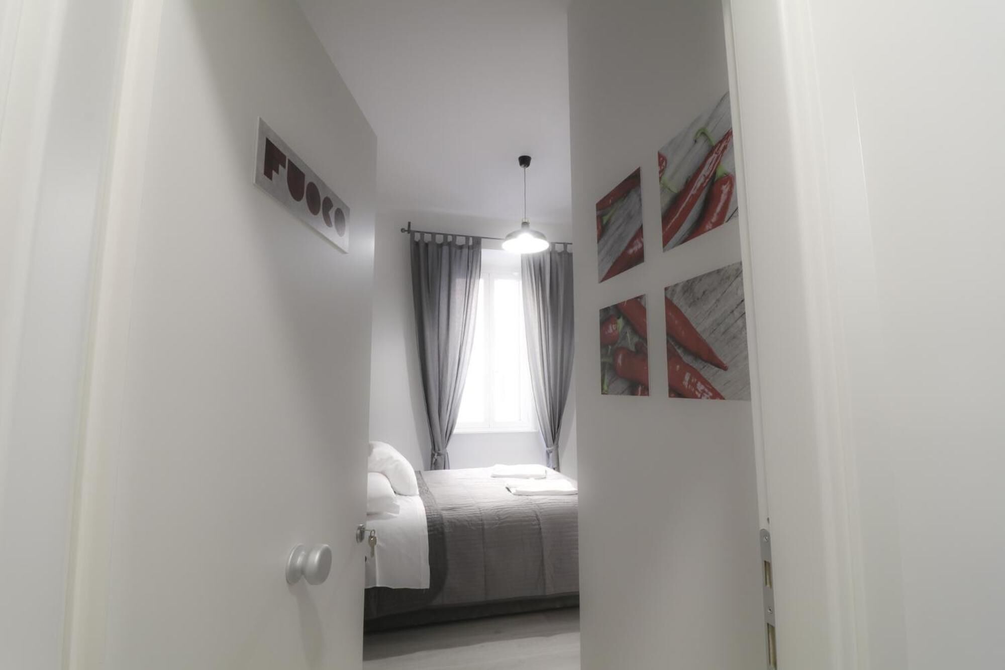 Een smalle gang die leidt naar een slaapkamer met een bed, een plafondventilator en een raam met gordijnen.