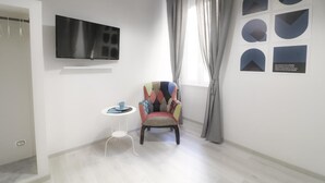 A modern living room with a flat-screen TV, a colorful armchair, a small side table, and a window with curtains. - Cinque Sogni (Rome)
