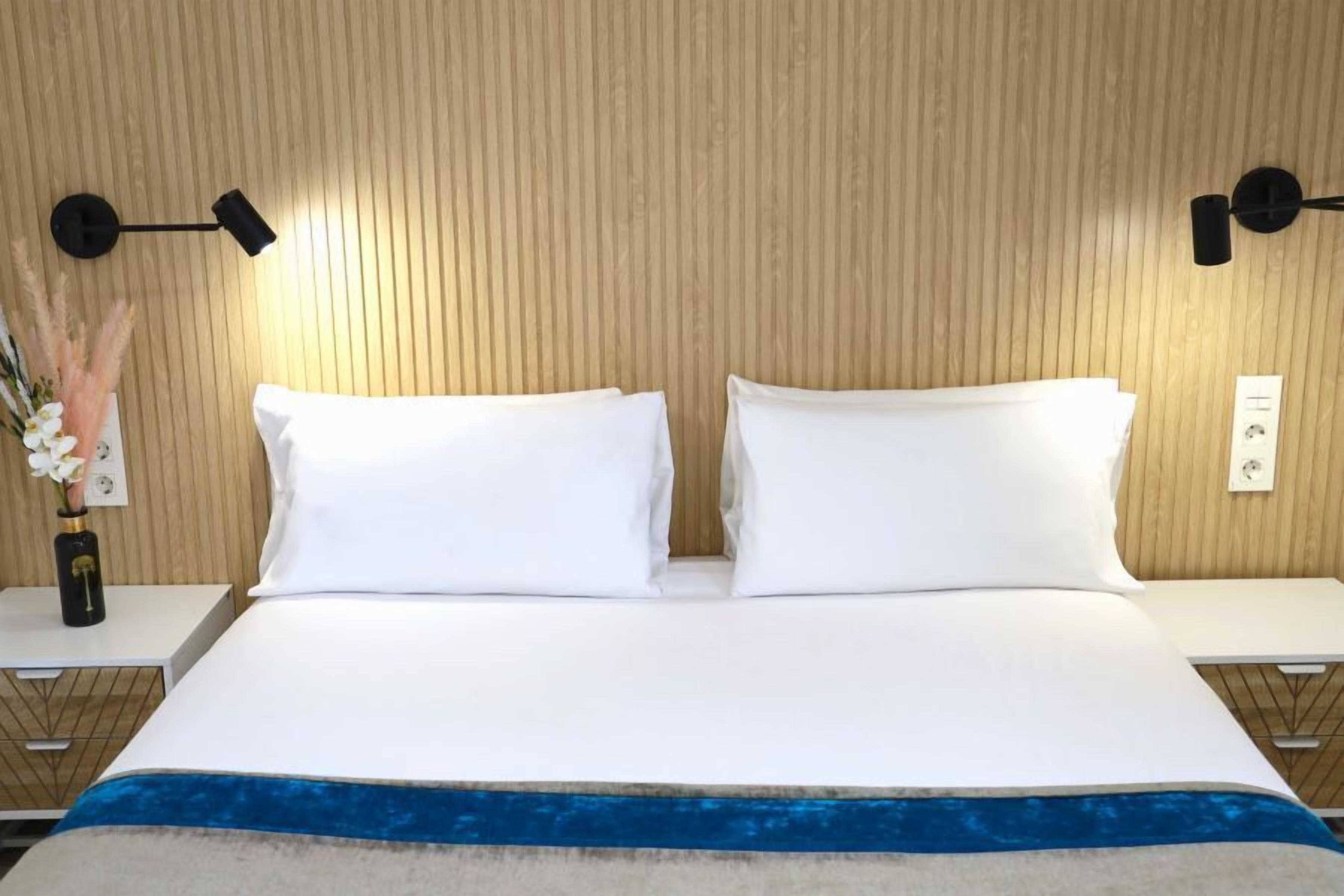 A neatly made bed with white linens, a blue accent at the foot, and two bedside tables with lamps.