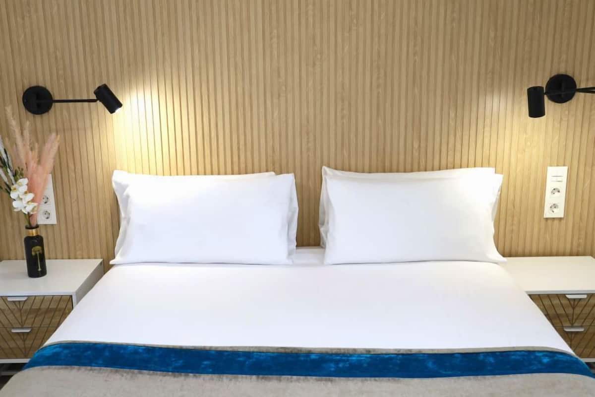 Un lit bien fait, avec du linge de lit blanc, une touche de bleu au pied du lit, et deux tables de chevet avec des lampes.