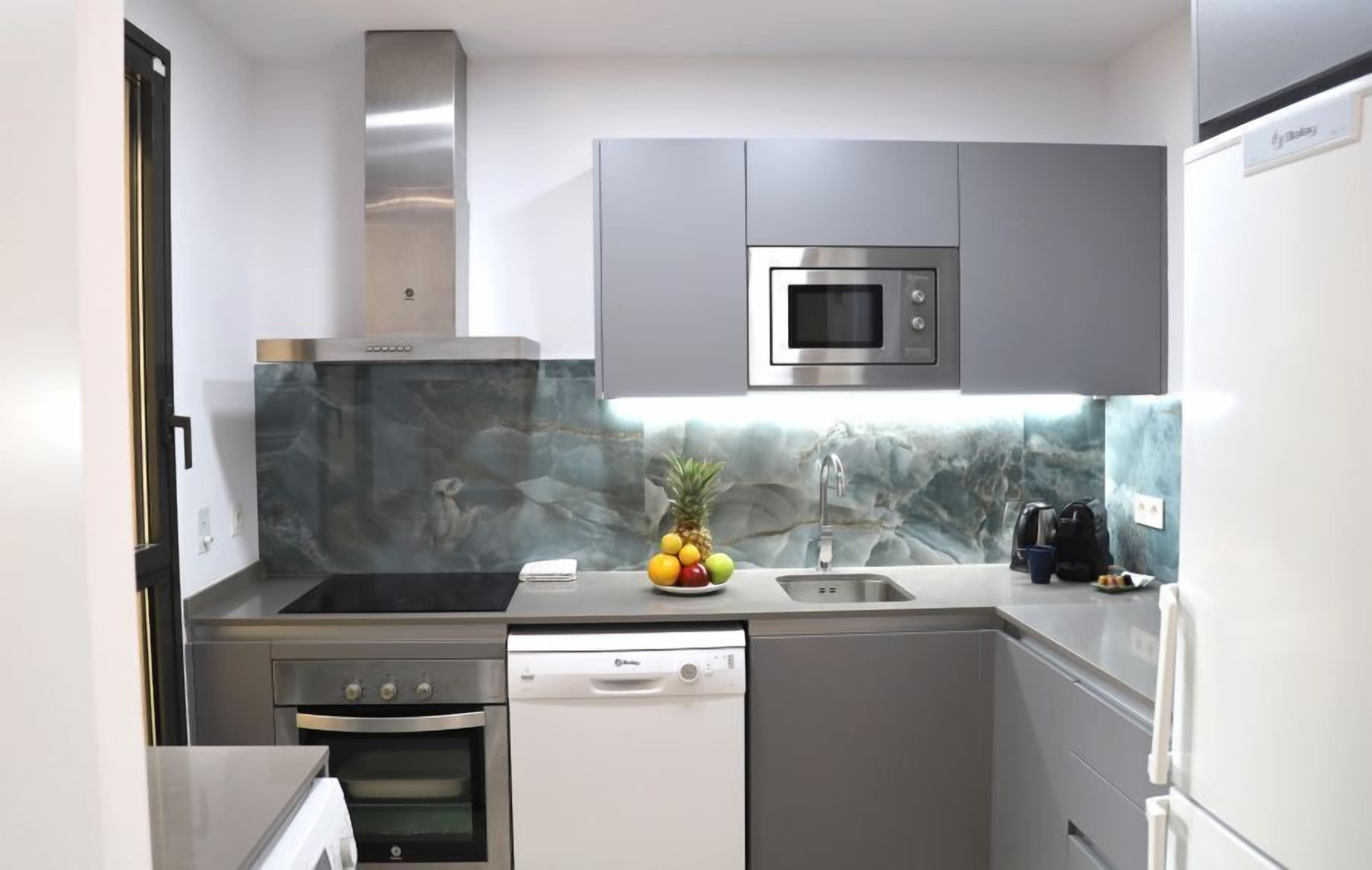 A compact kitchen with a stainless steel range hood, a built-in microwave, and a dishwasher.