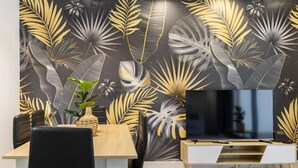 A modern living room with a flat-screen TV, a wooden dining table, and a decorative wall with a leaf pattern. - Cosmo Apartments Concell de Cent (Barcelona)