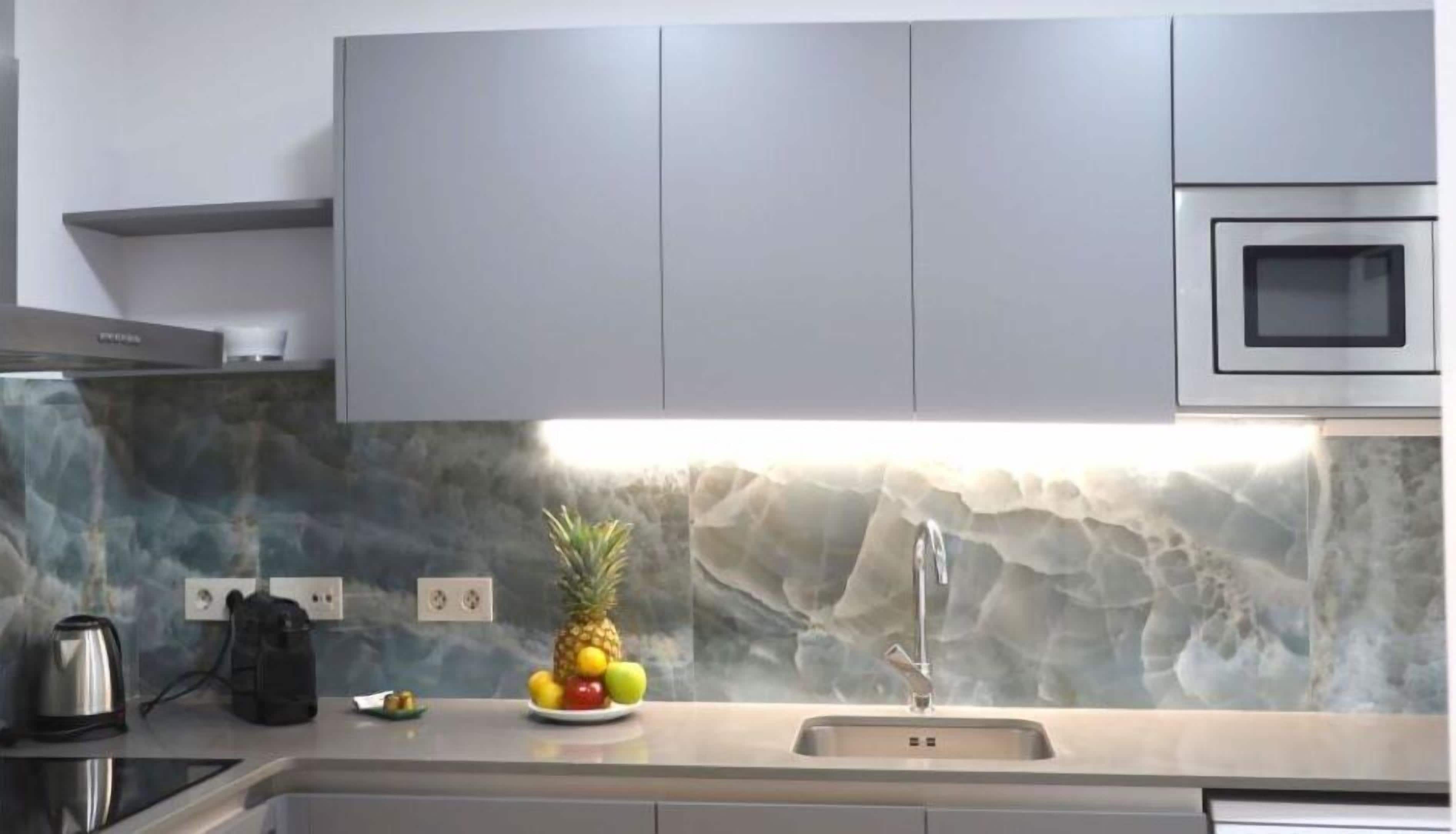 A modern kitchen with grey cabinets, a built-in microwave, and a granite backsplash.