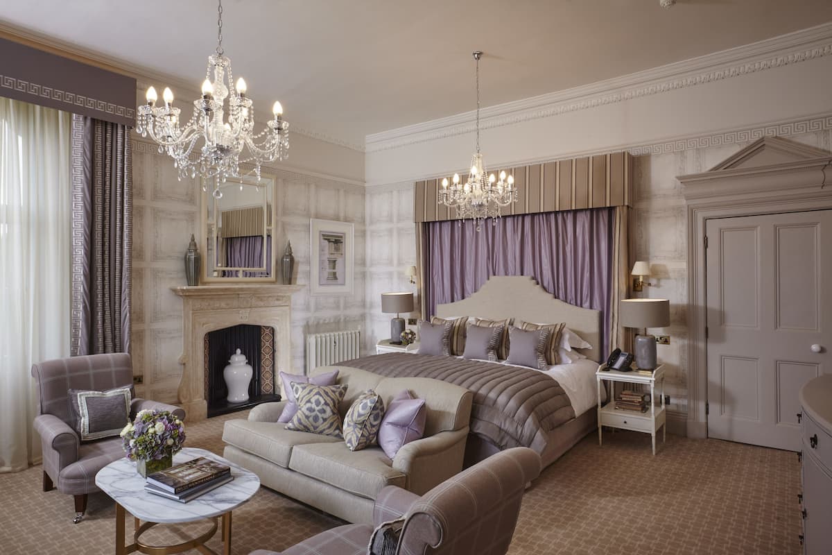 Un espacioso dormitorio con una cama grande, una zona de estar con sofá y sillón, chimenea y candelabro.