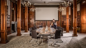 Un salón de conferencias con una gran mesa, sillas y una pantalla de proyector.