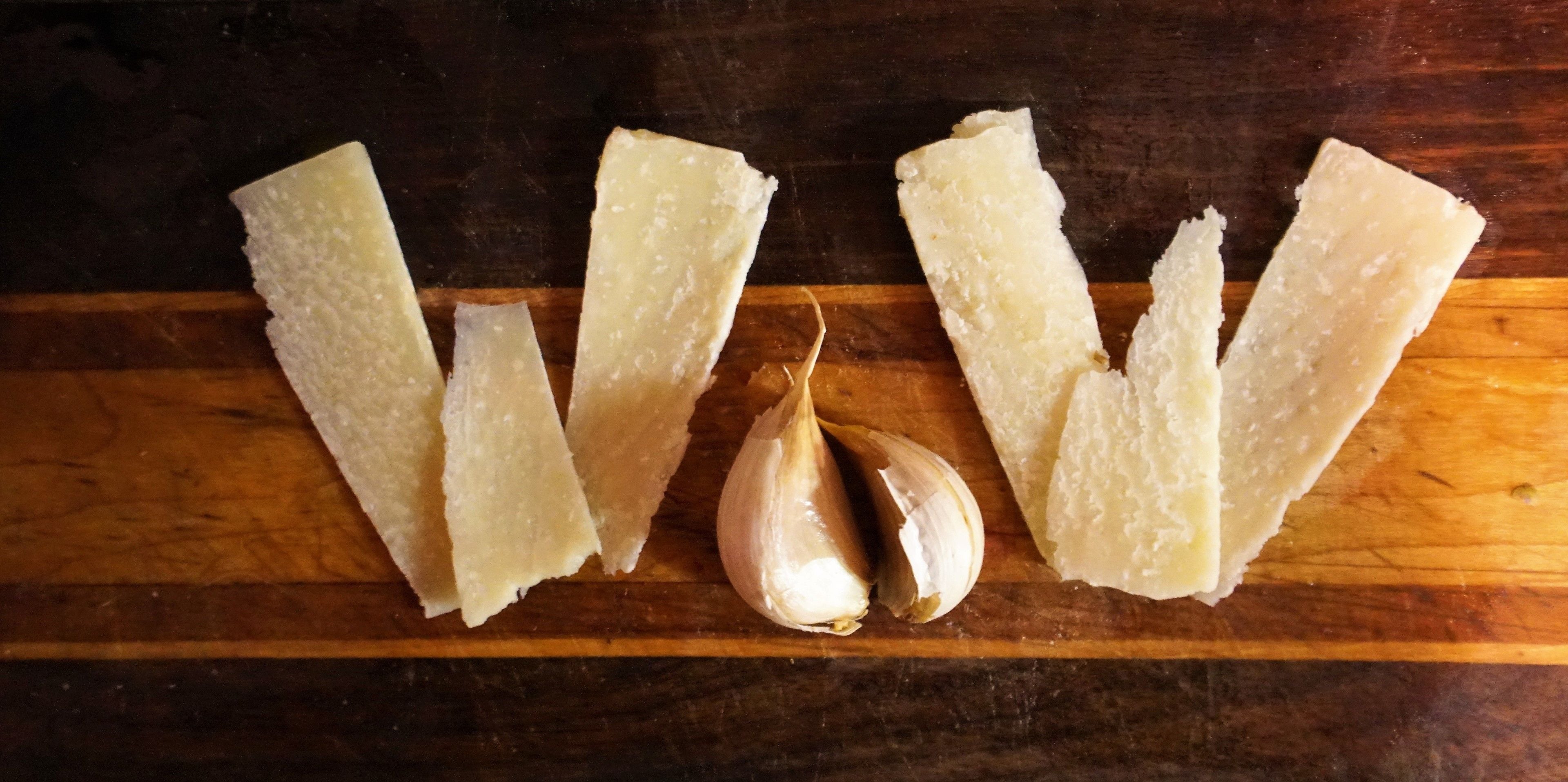 Varios trozos de queso blanco y un bulbo de ajo sobre una superficie de madera.
