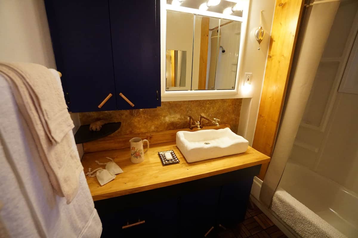 Un baño con tocador de madera, lavamanos blanco, espejo y una toalla colgada en la pared.