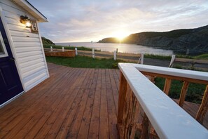 A wooden deck with a railing, a door, and a view of the ocean at sunset. - White On Wood (Crow Head)