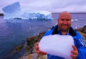 A person holding a large piece of ice in front of an iceberg. - White On Wood (Crow Head)