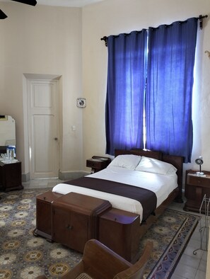 Un dormitorio con cama, mesita de noche, cómoda, silla y ventana con cortinas azules.