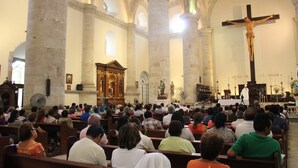 Interior de iglesia con techos altos, columnas de piedra y una gran cruz.