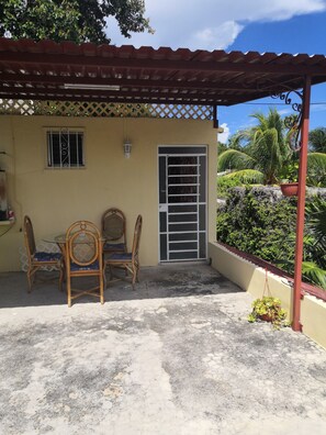 Un espacio de patio cubierto con una mesa y dos sillas, una ventana con rejas y una puerta con portón metálico.