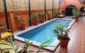 Un espace piscine agrémenté de plantes en pot, un coin salon et un sol carrelé.