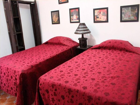 Une chambre avec deux lits, chacun recouvert d’une couverture à motifs floraux rouges. Une lampe noire se trouve sur une petite table placée entre les deux lits.