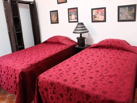 A room with two beds, each covered with a red floral bedspread. There is a black lamp on a small table between the beds.
