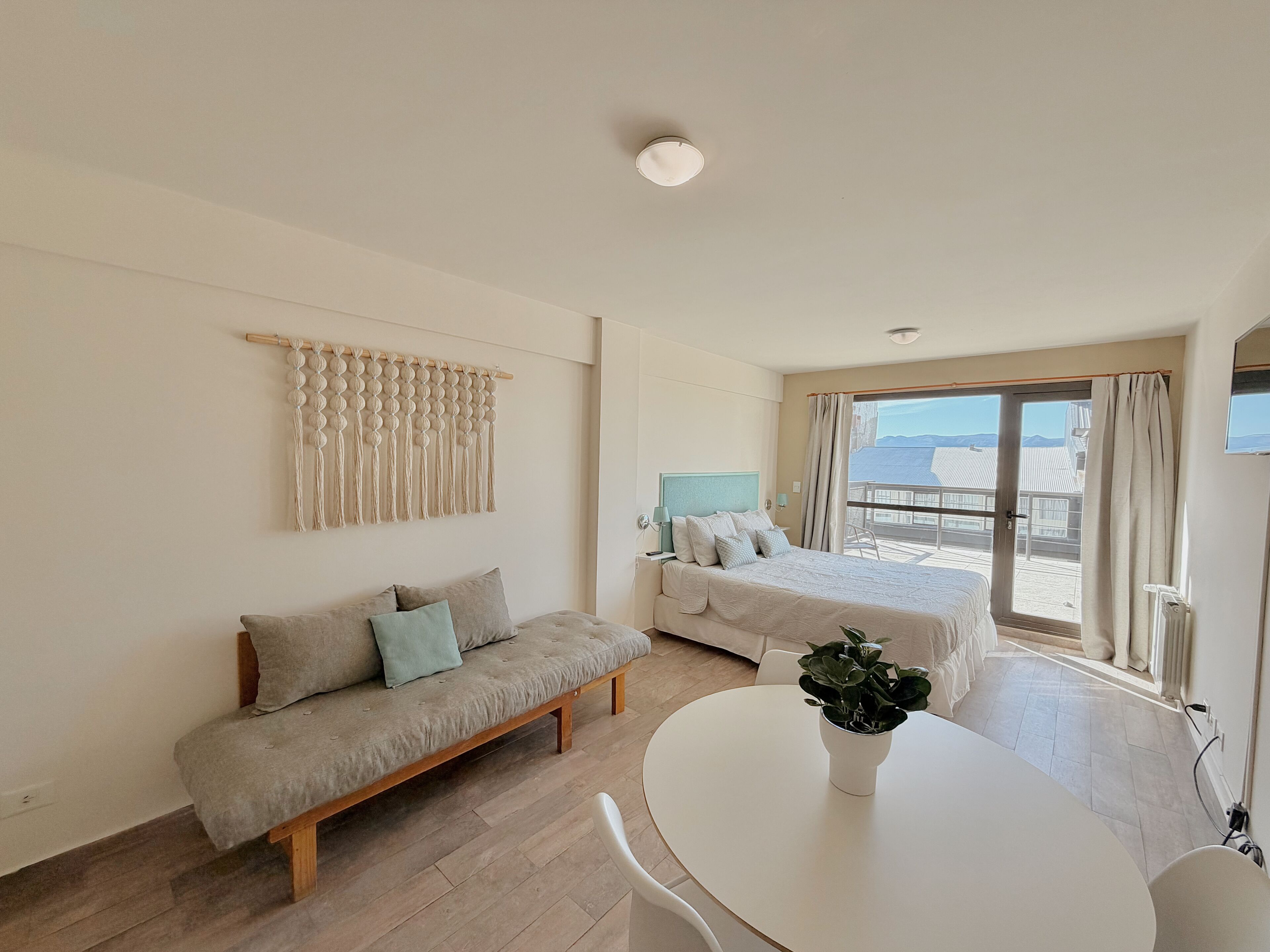 A hotel room with a bed, a sofa, a dining table, and a view of the sea.