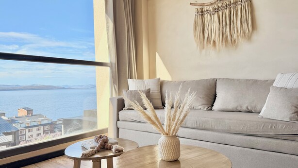 Una sala de estar moderna con vista al mar, un sofá, una mesita redonda y un tapiz decorativo.