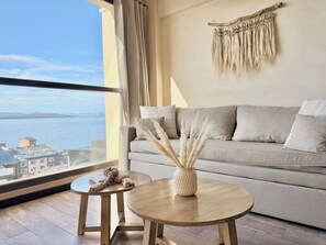 Una sala de estar moderna con vista al mar, un sofá, una mesita redonda y un tapiz decorativo.