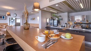 A breakfast bar with a variety of food items, a clock, and a modern kitchen in the background. - B&B HOTEL La Rochelle Centre (La Rochelle)