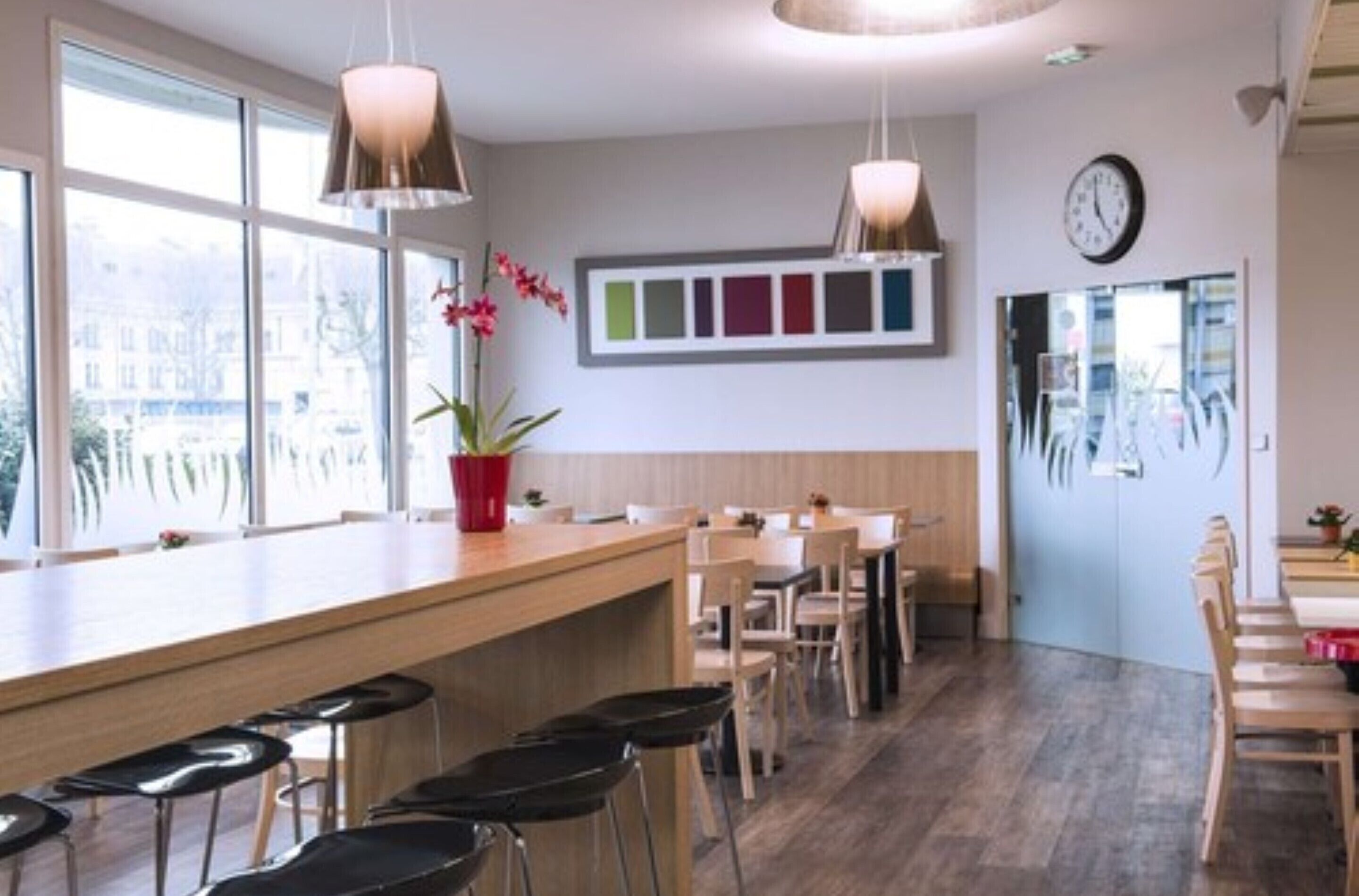 A modern bar area with wooden bar stools, pendant lighting, and a view of the city through large windows.