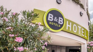 A B&B hotel sign with a green and yellow color scheme, surrounded by pink flowers and greenery. - B&B HOTEL La Rochelle Centre (La Rochelle)