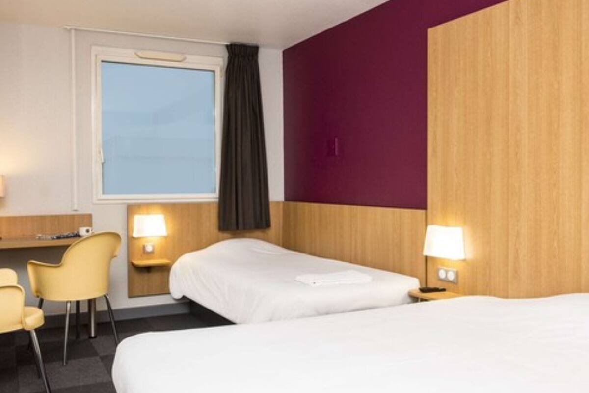 A hotel room with two beds, a desk, a chair, and a window with curtains.