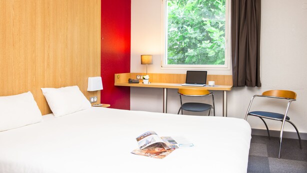 A hotel room with a bed, a desk with a laptop, a chair, and a window with curtains. - B&B HOTEL La Rochelle Centre (La Rochelle)