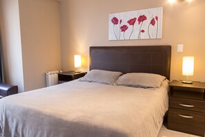 A neatly made bed with a headboard, two bedside tables with lamps, and a wall-mounted artwork of red flowers.
