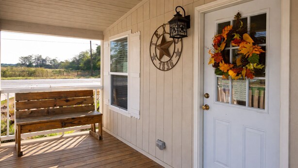 A wooden bench on a porch, a white door with a decorative wreath, and a wall-mounted star-shaped decoration. - Shale Lodge Pleasanton (Pleasanton)