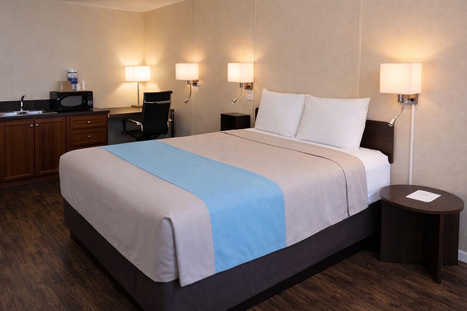 A hotel room with a bed, bedside tables, a desk with a chair, a microwave, and a sink.