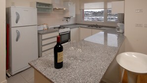 Una cocina con refrigerador, horno, lavamanos y ventana con vista a un estacionamiento.
