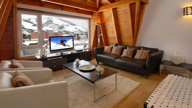 Una sala de estar acogedora con televisor, sofá de cuero y vistas a montañas nevadas a través de amplias ventanas.