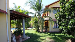 Um jardim bem cuidado com piscina, um alpendre coberto e um edifício de dois andares com telhado de azulejos.