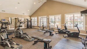Un gimnasio con equipo de ejercicio variado, ventanas amplias y un techo alto.
