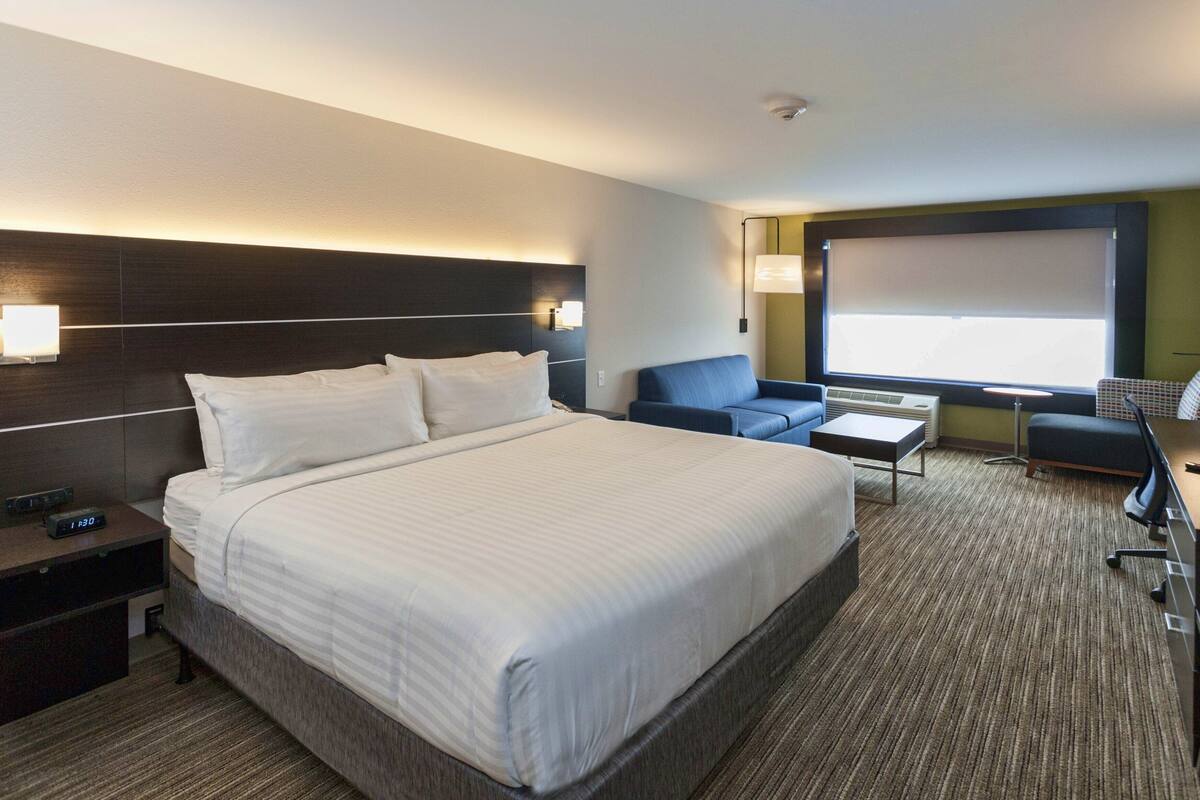 Una habitación de hotel con una cama grande, un escritorio, una silla, un sofá y un televisor.