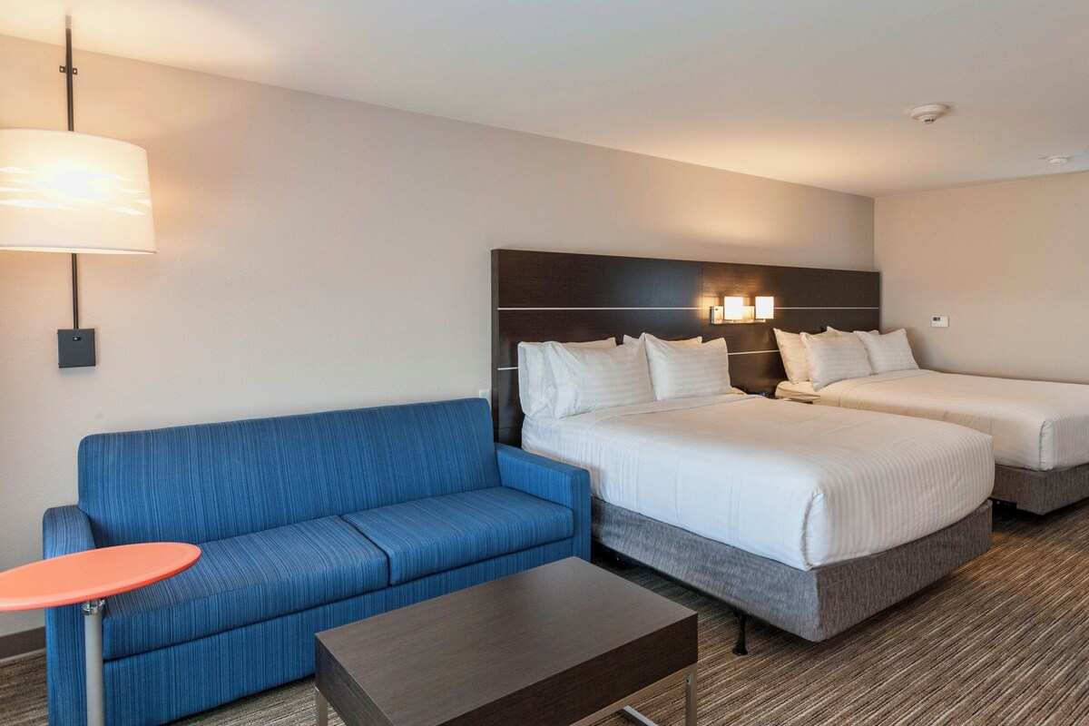 Une chambre d’hôtel avec deux lits, un canapé bleu, une petite table et une lampe.