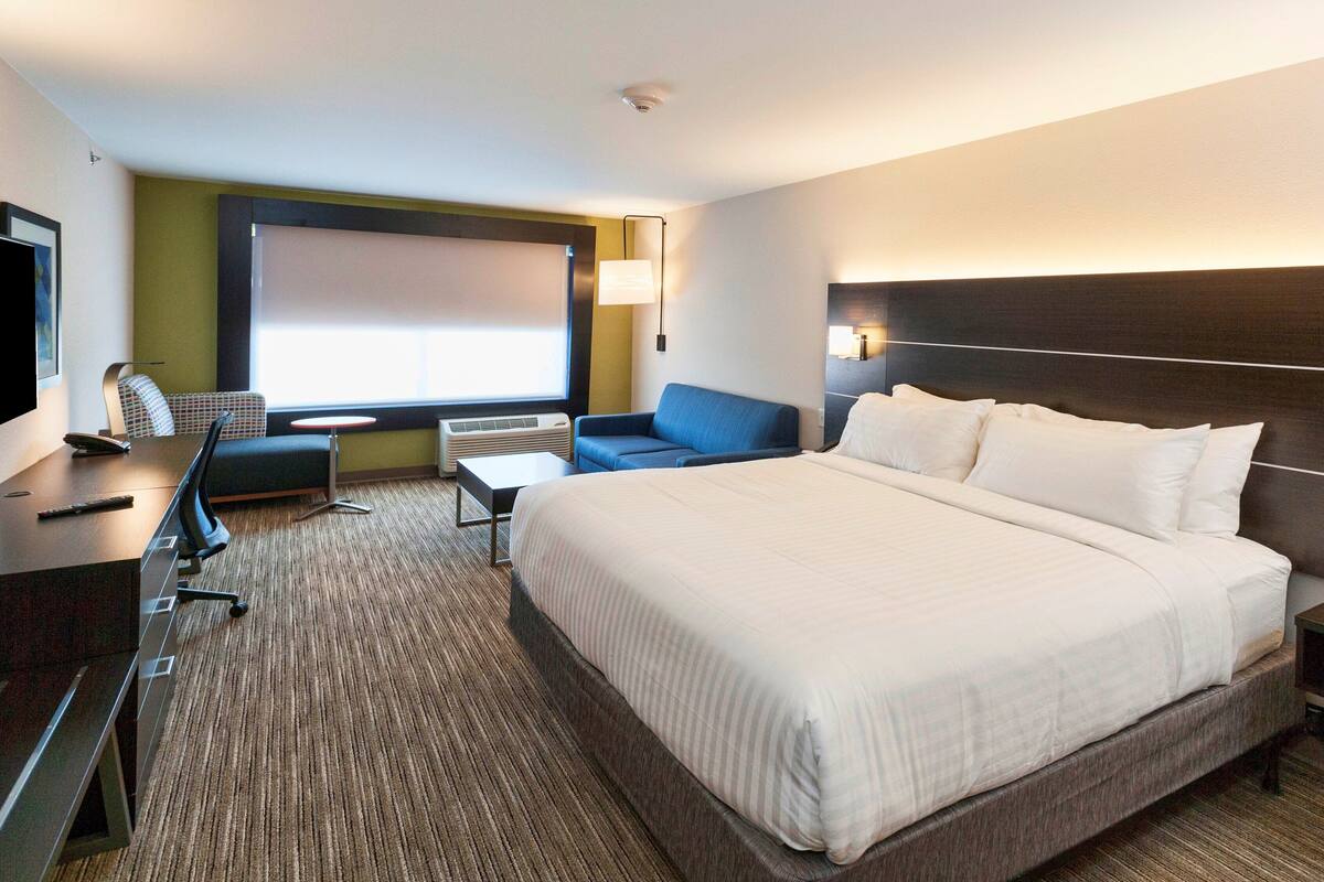 Una habitación de hotel con una cama grande, un escritorio con silla, un sofá y un televisor.