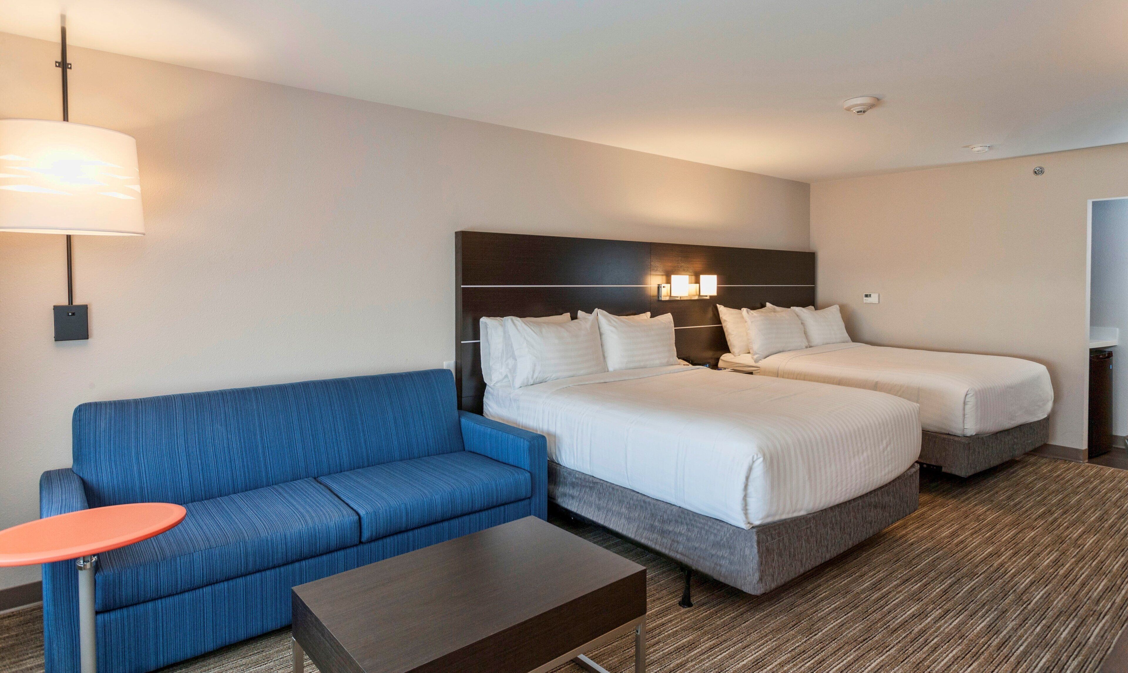 A hotel room with two beds, a blue sofa, a small table, and a lamp.
