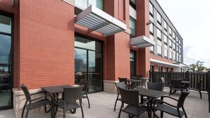 Un patio al aire libre con mesas y sillas, un edificio de ladrillo y una entrada de vidrio.