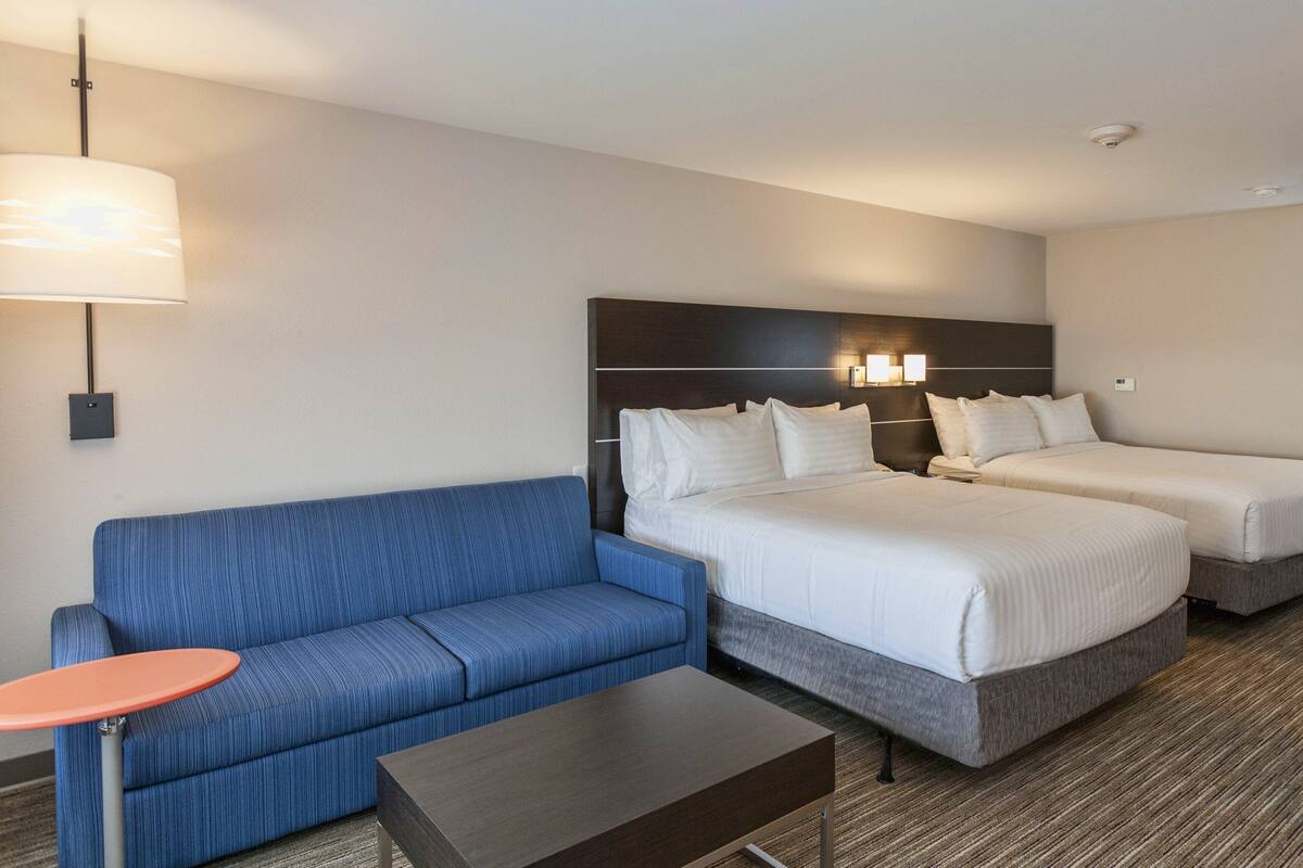 Una habitación de hotel con dos camas, un sofá azul, una mesita y una lámpara.