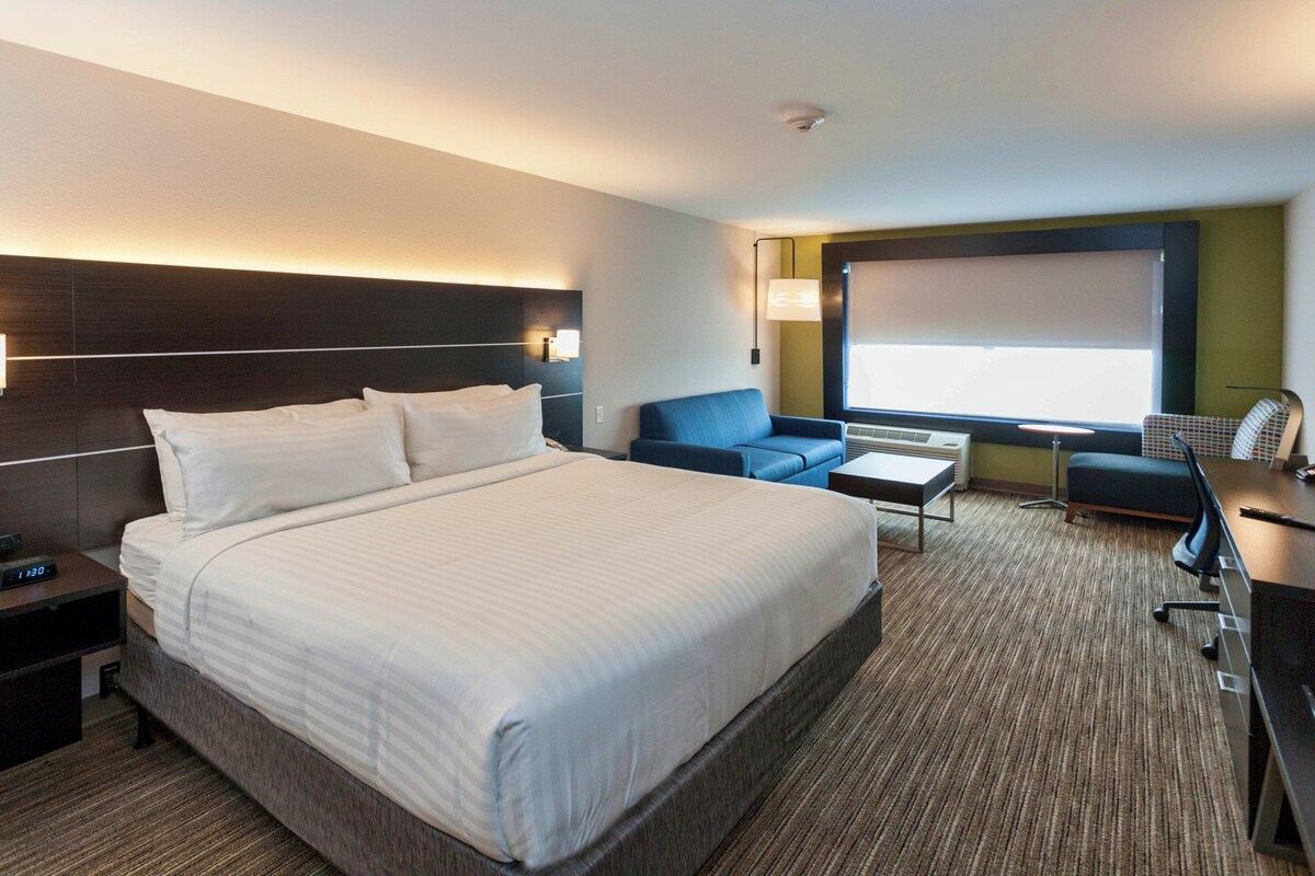 Une chambre d’hôtel avec un grand lit, un bureau, une chaise, un canapé et une télévision.
