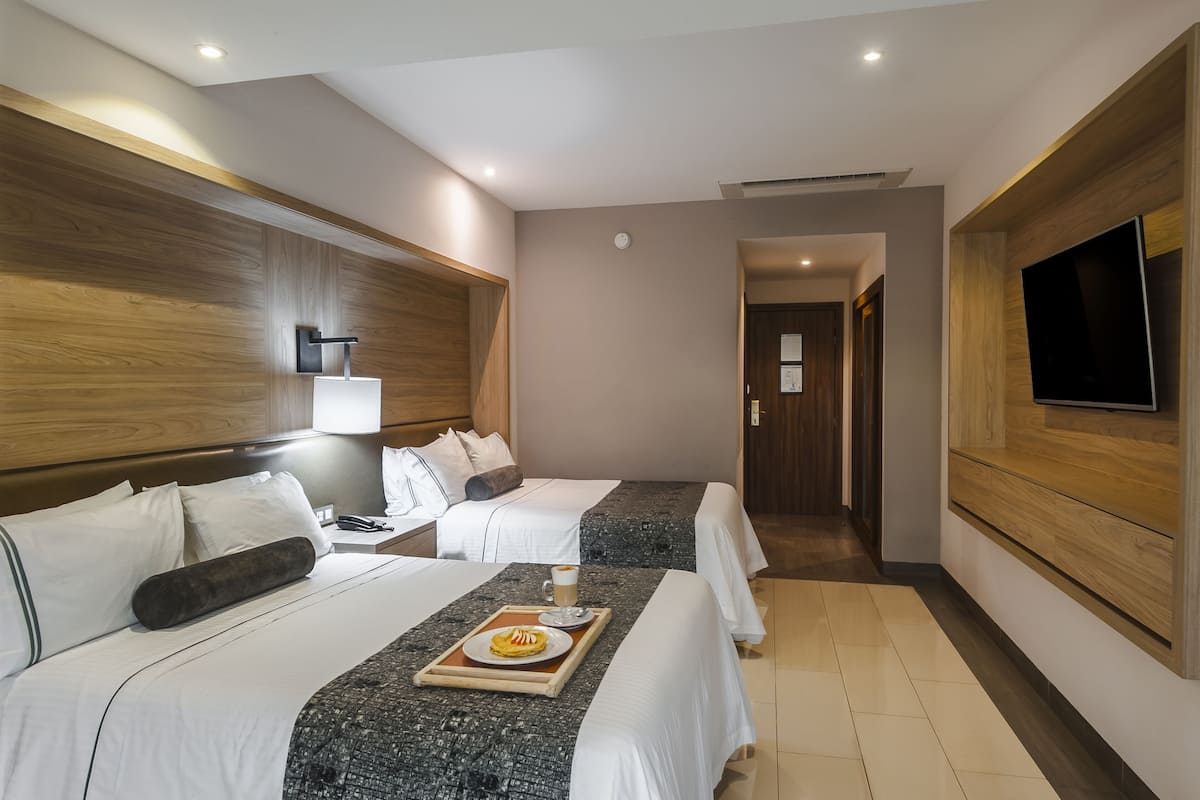 Een hotelkamer met twee bedden, een aan de muur bevestigde televisie en een dienblad met ontbijt op het bed.