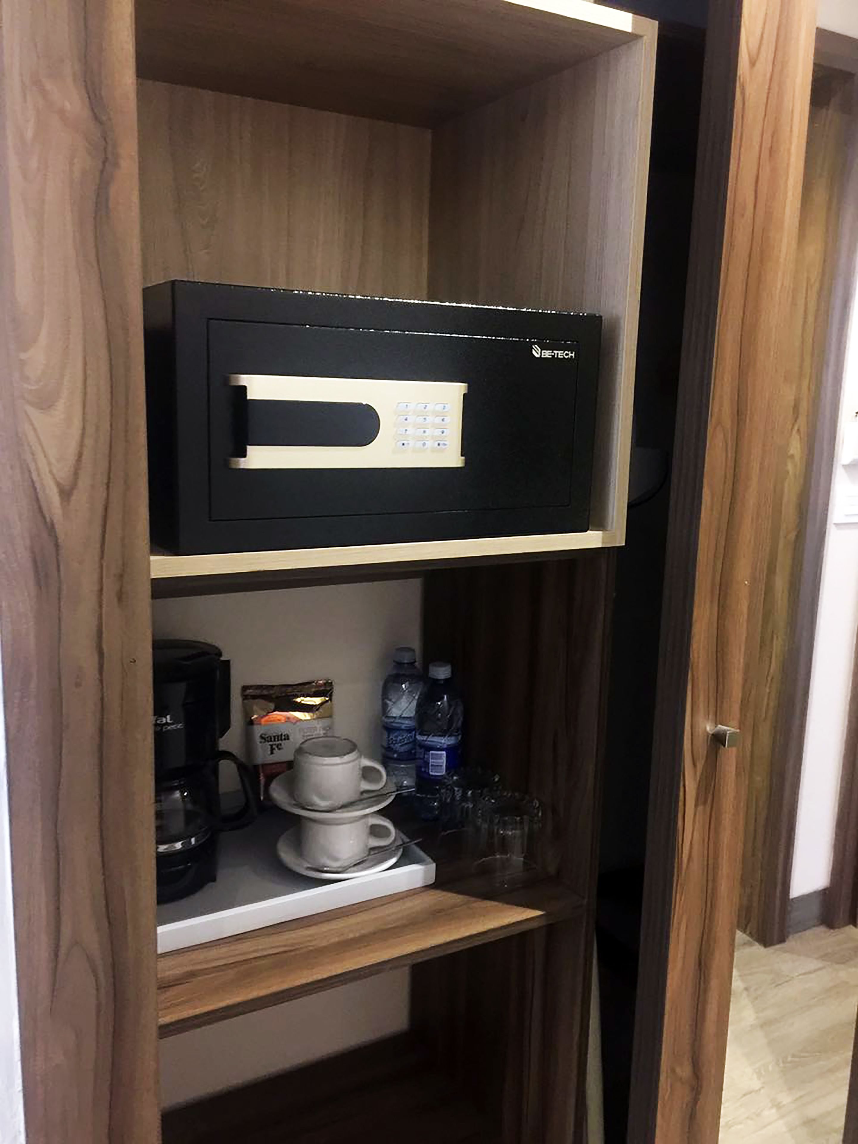 A minibar with a coffee maker, a water bottle, and a cup on a shelf.