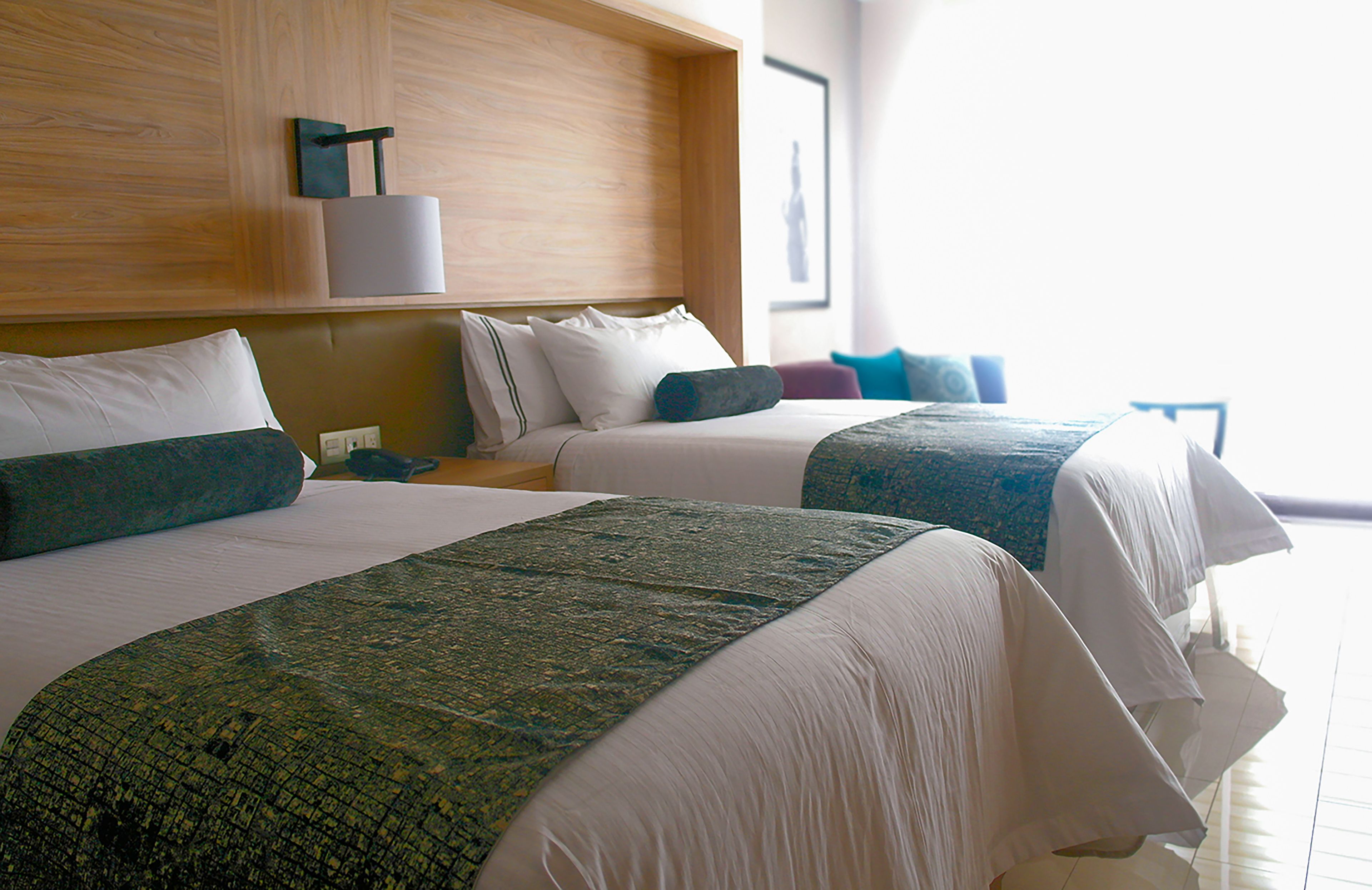 A hotel room with two beds, a wooden headboard, a nightstand, and a window with a view.