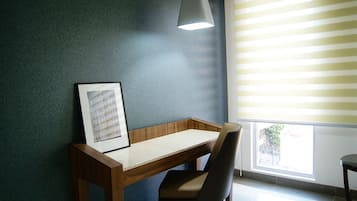 Una habitación con escritorio, silla, un cuadro enmarco y una ventana con persianas.