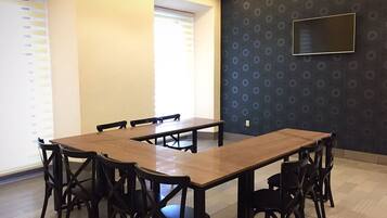 A conference room with a long table and chairs, a TV on the wall, and windows with blinds.