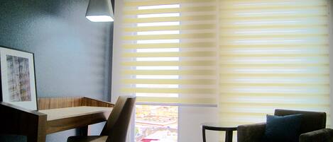A room with a desk, a chair, a sofa, and a large window with blinds.