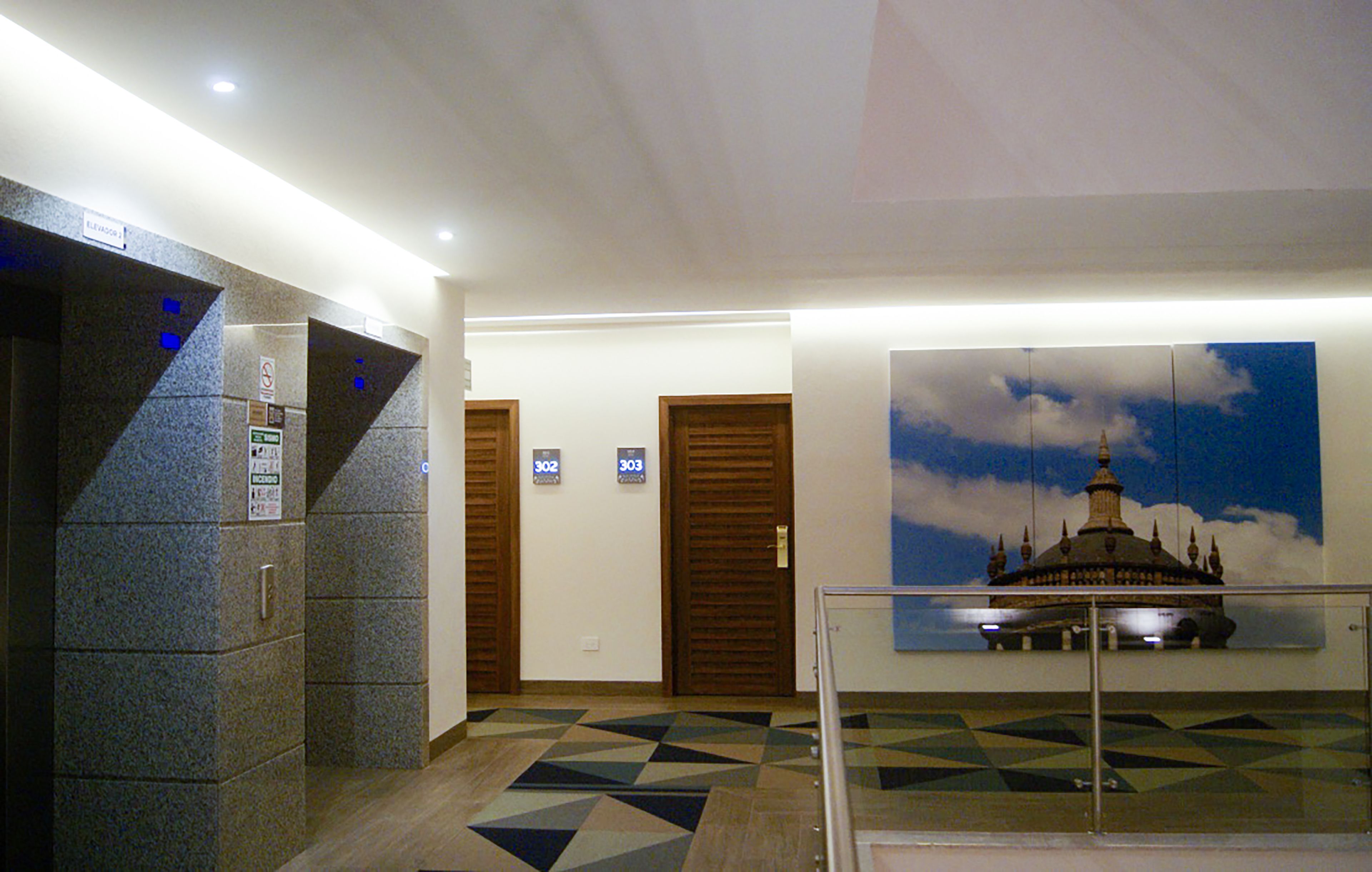 Un hall d’hôtel doté d’un sol à motifs géométriques, d’une rambarde en verre et d’une œuvre d’art murale représentant un bâtiment.