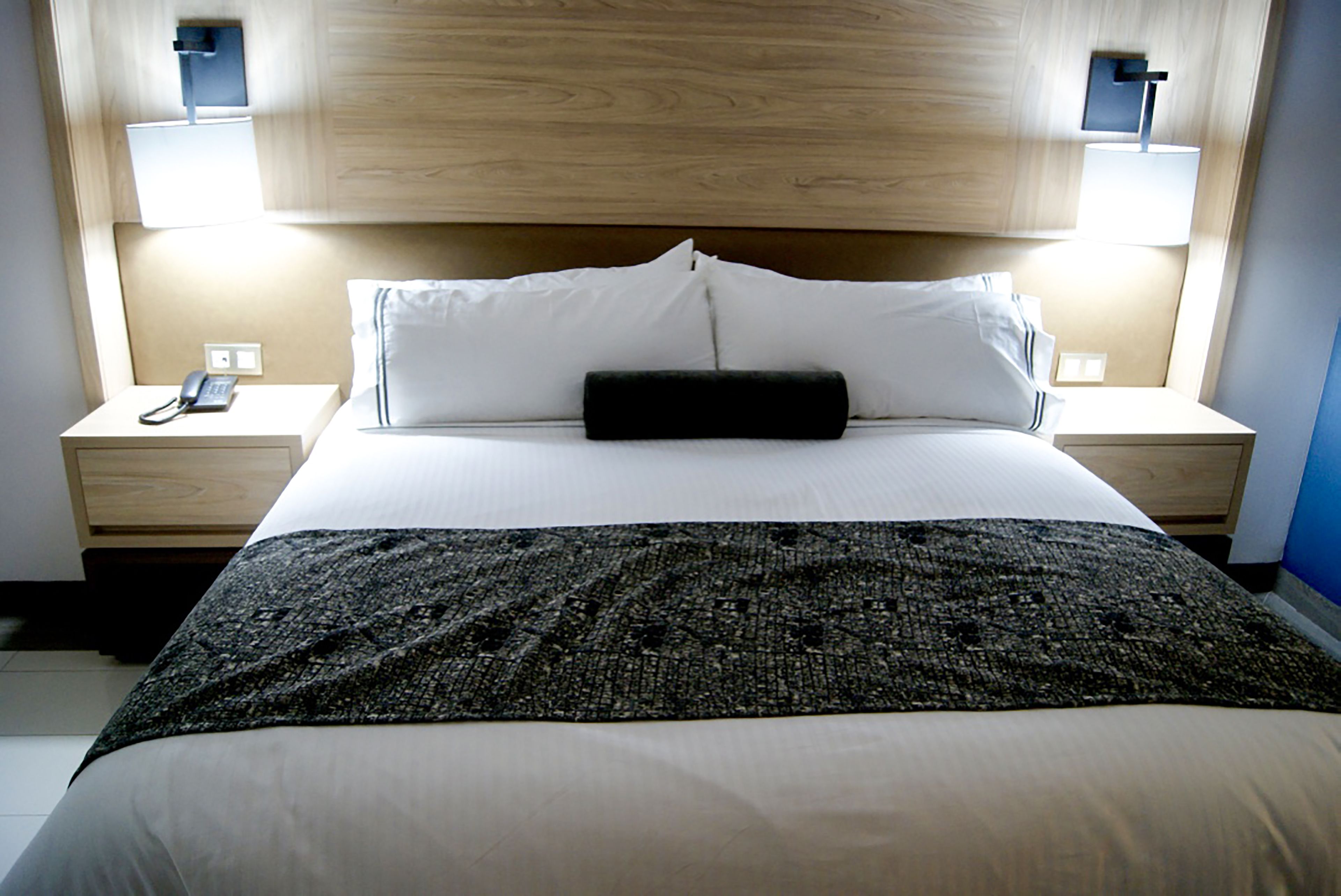 Una habitación de hotel con una cama grande, dos mesitas de noche con lámparas y un cabecero de madera.