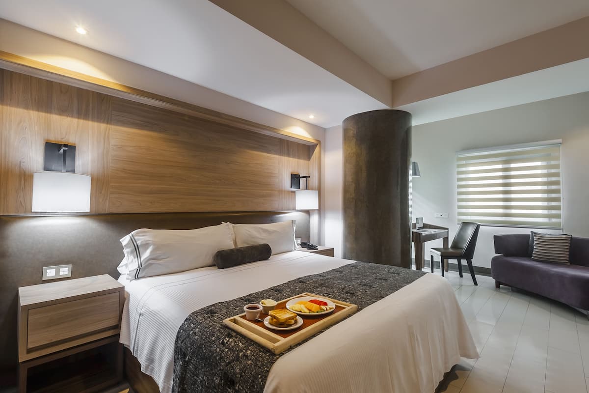 Een moderne hotelkamer met een groot bed, nachtkastje, bureau, bank en een ontbijtplateau.